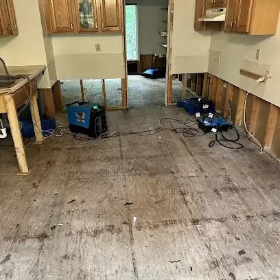 Kitchen with the floor covering removed and air movers blowing along the cabinet bases